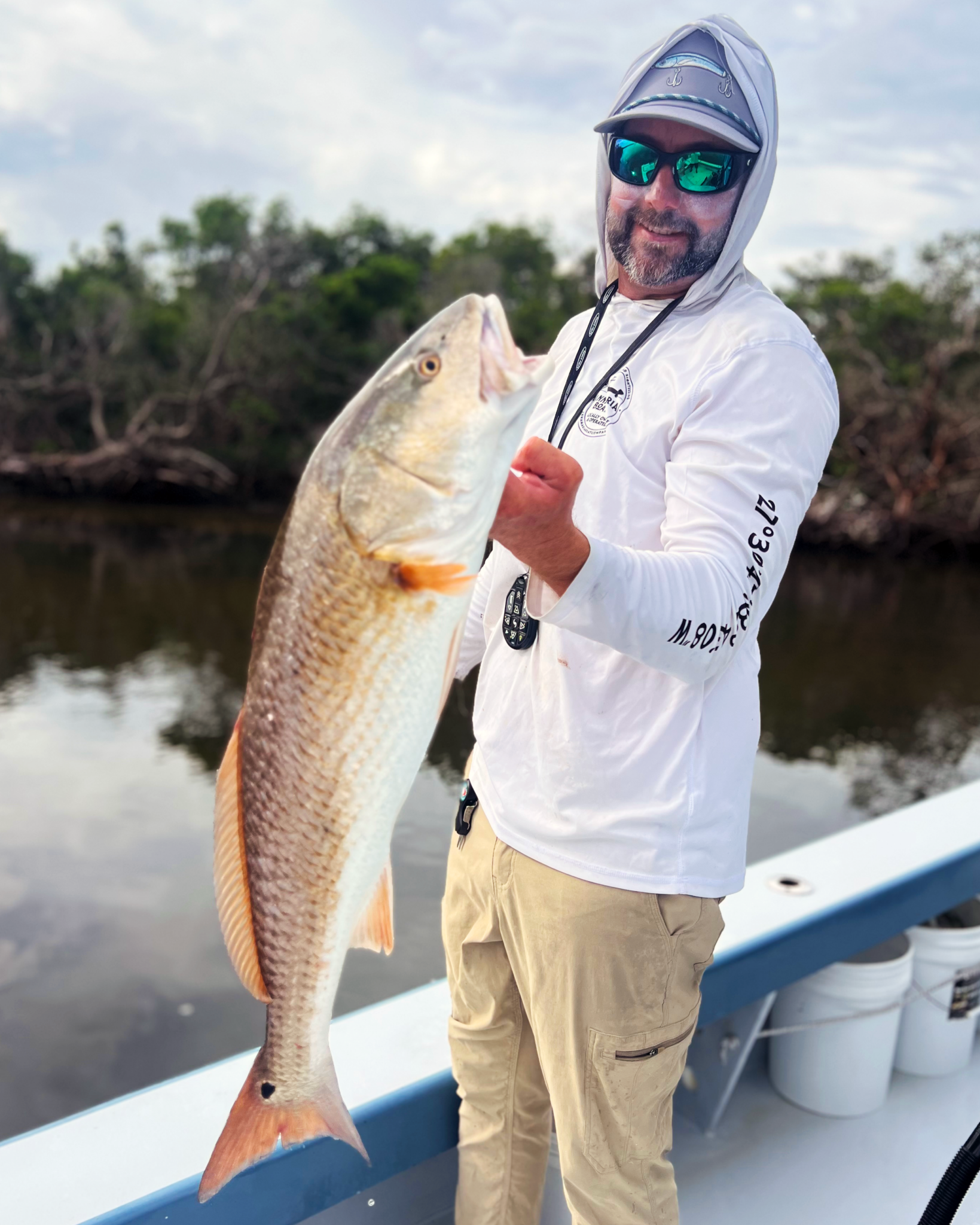 A man on a boat holding a big, slightly red colored fish