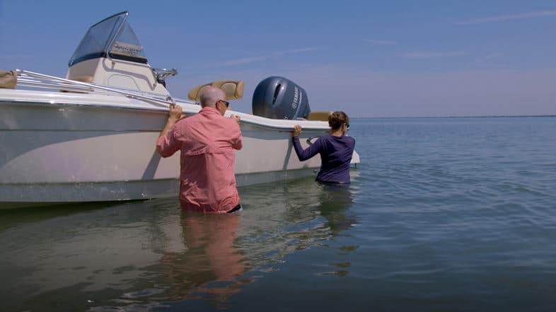 Two people standing in water pushing a boat